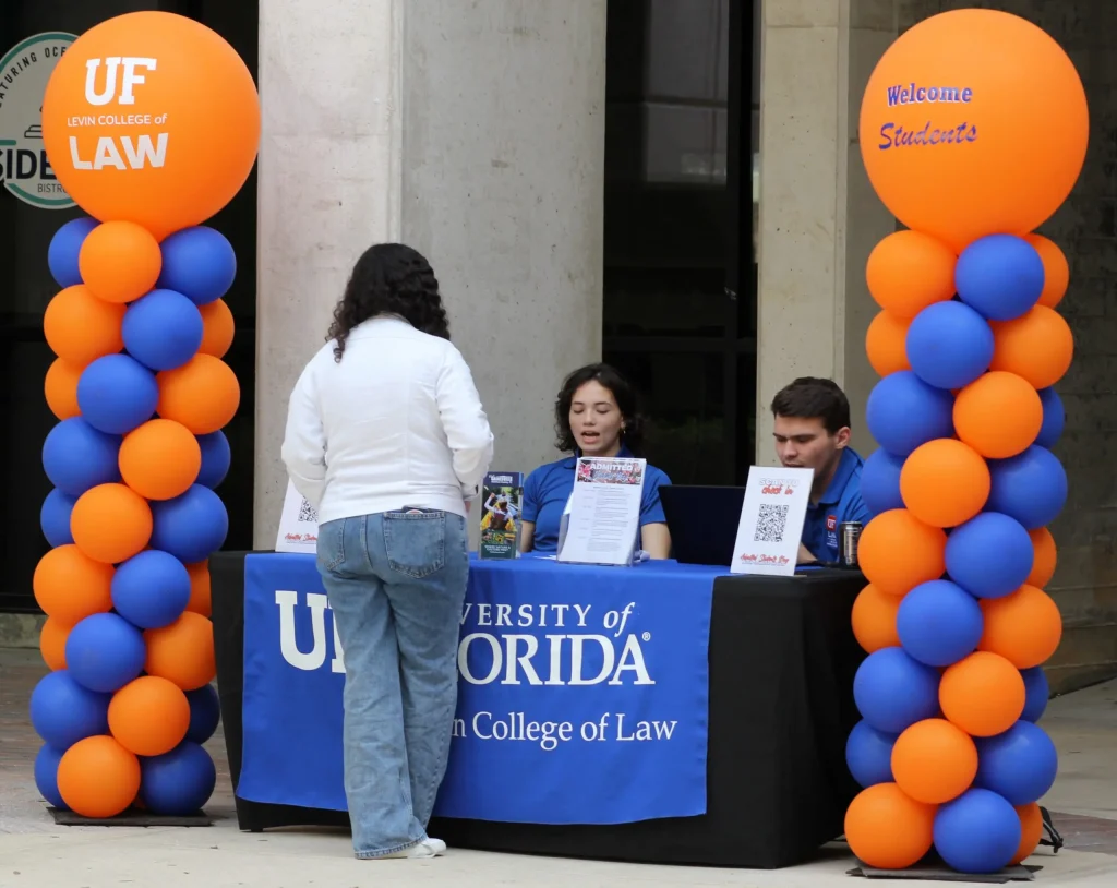 An individual standing in front of a UF Levin College of Law table flanked with blue and orange balloon towers