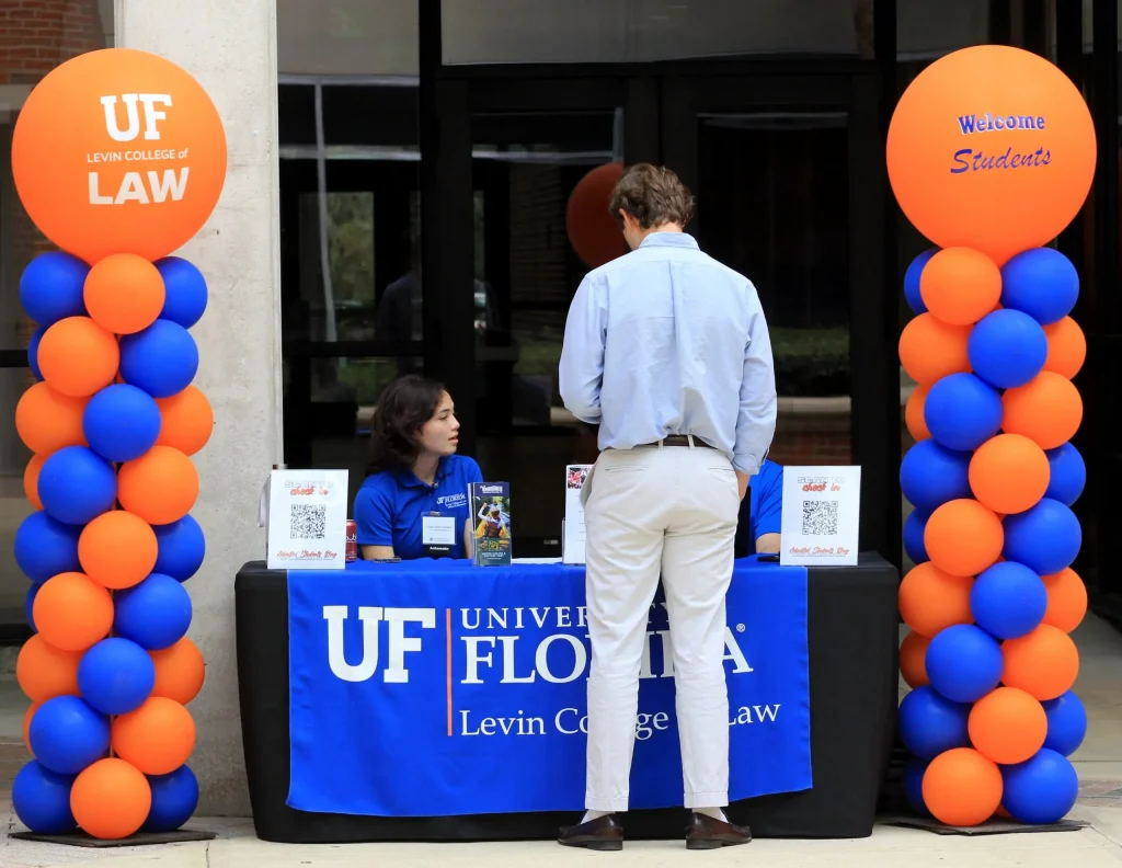 An individual standing in front of a UF Levin College of Law table flanked with blue and orange balloon towers