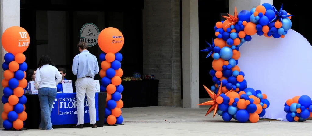 Individuals standing an UF table flanked by balloons next to orange and blue balloon photo backdrop