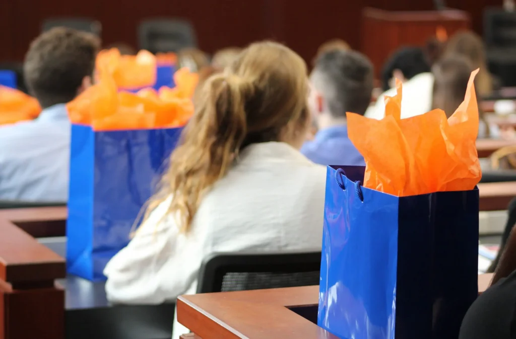 Event attendees from behind with blue giftbags on table in front of them