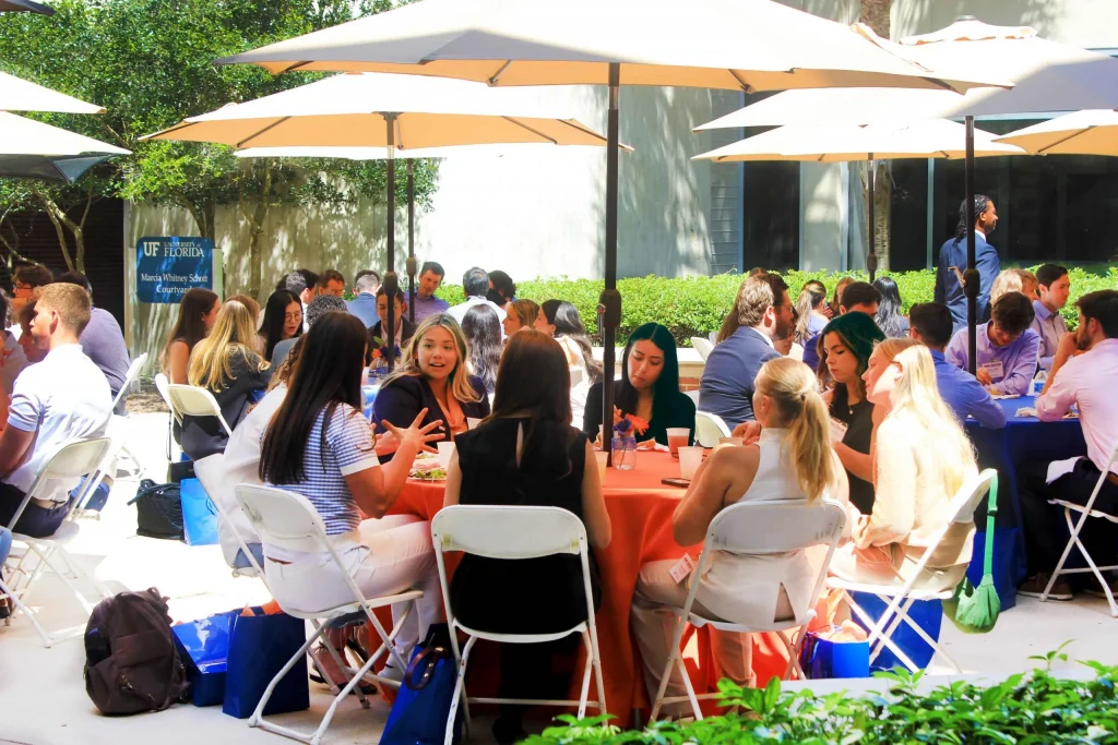 Event attendees sit at outdoor tables under umbrellas