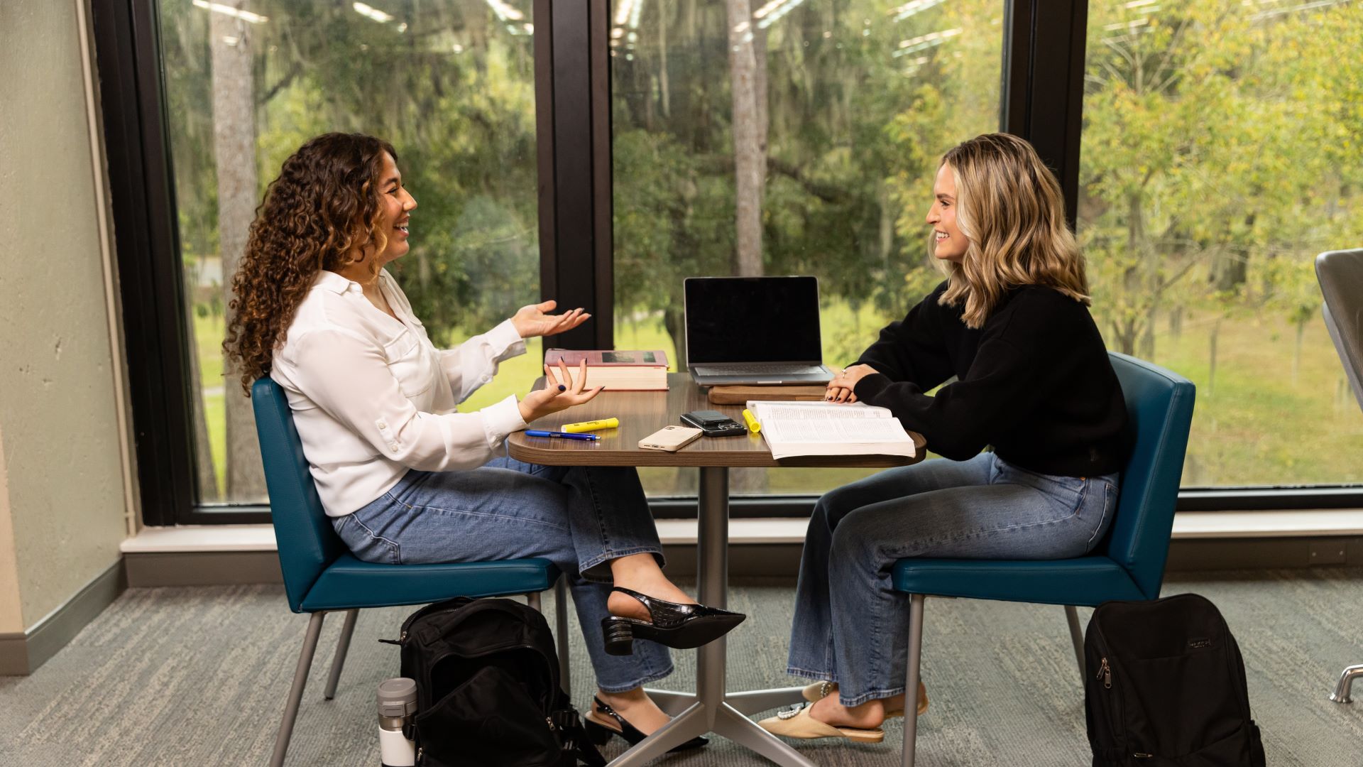 Two individuals sit across a table from each other in conversation