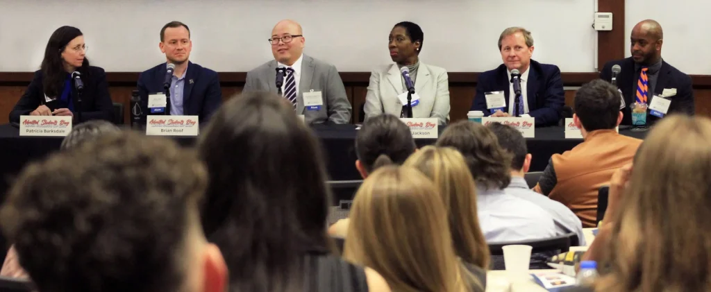 Six panelists speak to the event crowd at the front of the room