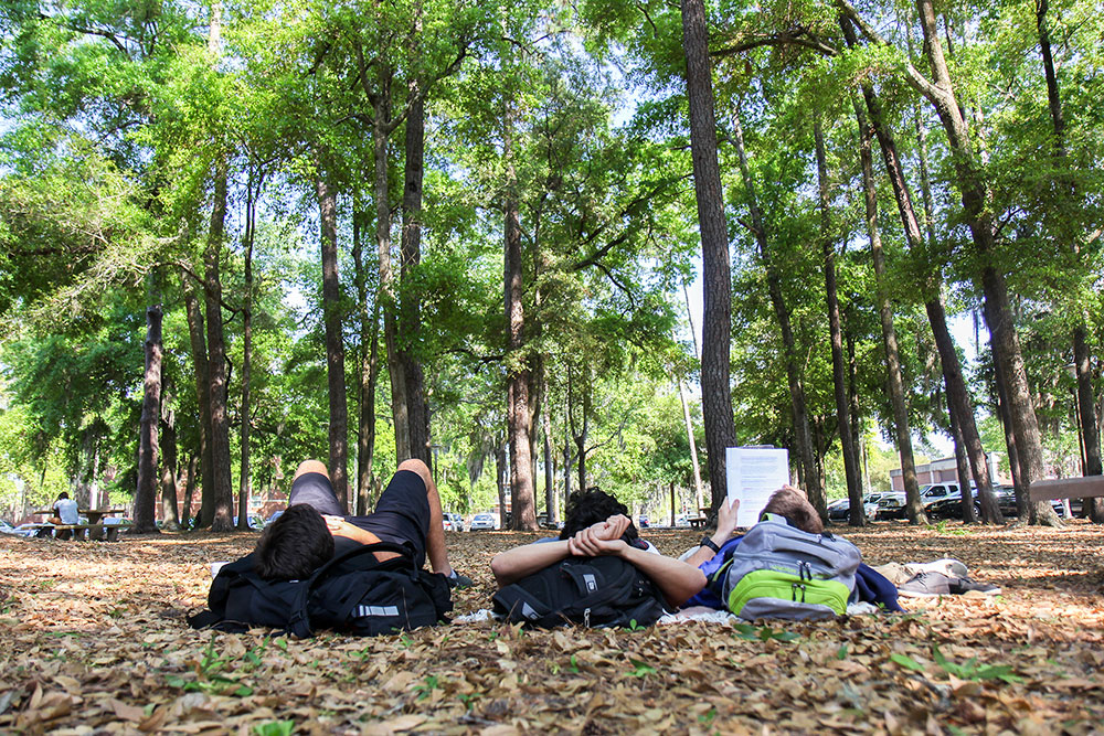Three students lay on their backs in the grass, using backpacks as pillows
