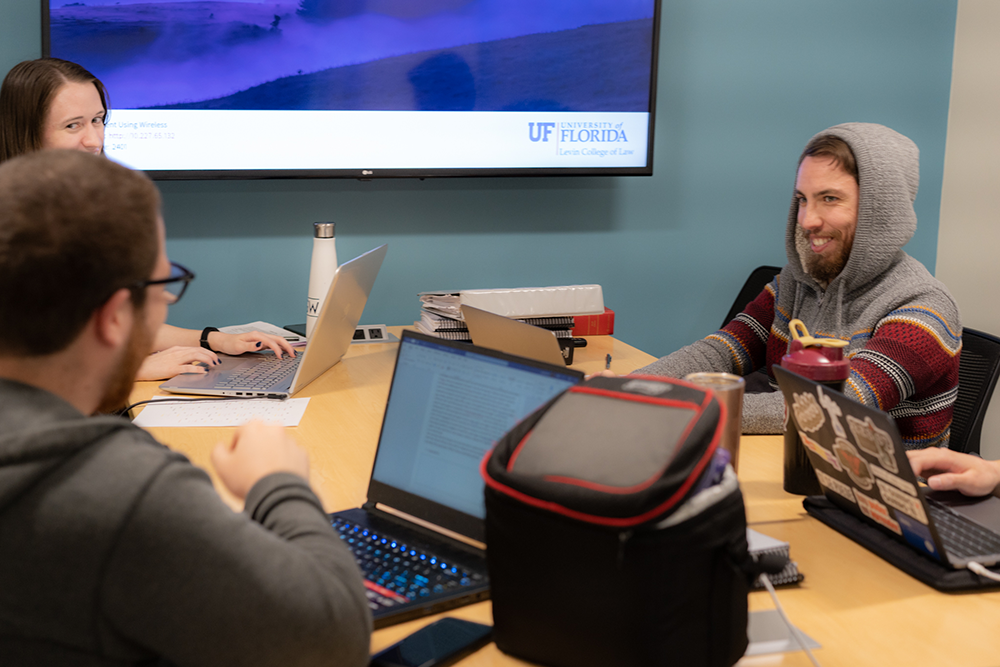 Students sit around a table working on laptops in a study room