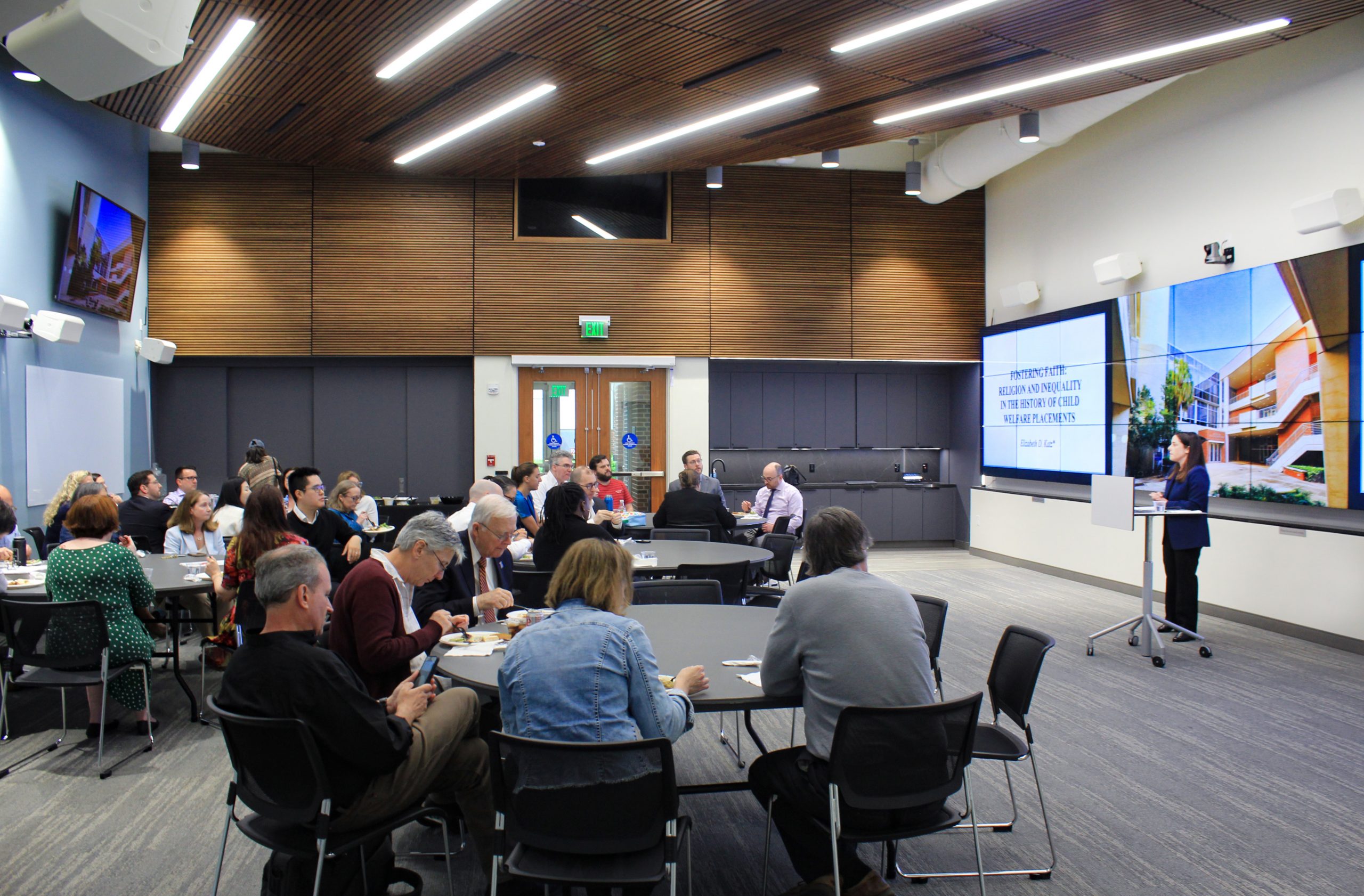 UF Law Professor Elizabeth D. Katz stands at the front of a room and gives a presentation to other faculty members. Her presentation title is "Fostering Faith: Religion and Inequality in the History of Child Welfare Placements".